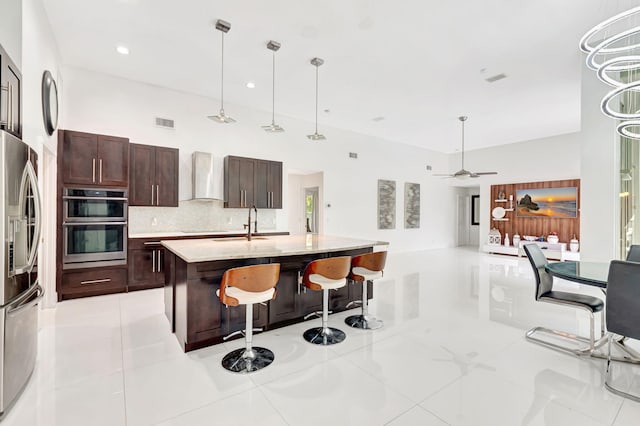 kitchen with wall chimney exhaust hood, tasteful backsplash, visible vents, appliances with stainless steel finishes, and a kitchen bar