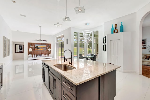 kitchen with arched walkways, dishwasher, hanging light fixtures, light stone countertops, and a sink