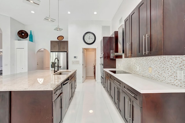 kitchen featuring arched walkways, a sink, backsplash, and dark brown cabinets