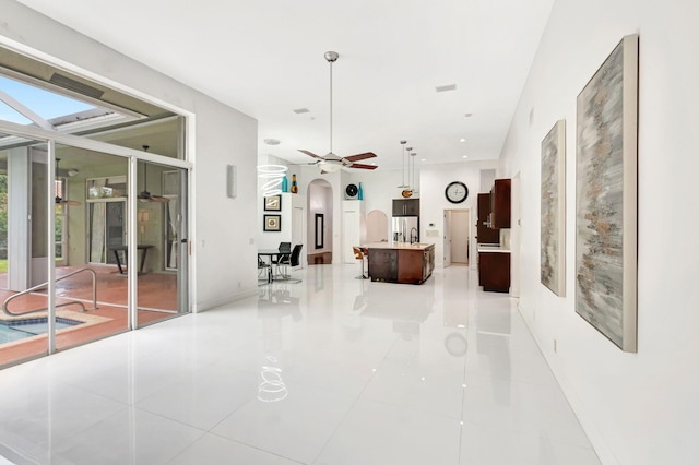 interior space featuring arched walkways, stainless steel fridge with ice dispenser, ceiling fan, a kitchen island with sink, and light countertops