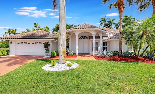 mediterranean / spanish home with an attached garage, a tile roof, driveway, stucco siding, and a front lawn