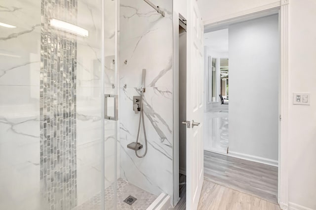 full bathroom with a marble finish shower, baseboards, and wood finished floors