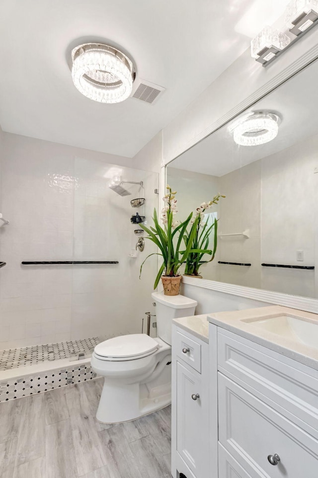 full bath with visible vents, a tile shower, vanity, and toilet