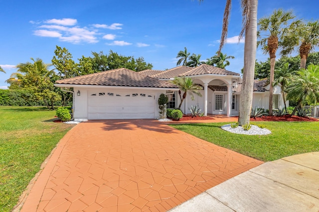 mediterranean / spanish-style home featuring a garage, a tiled roof, concrete driveway, stucco siding, and a front lawn