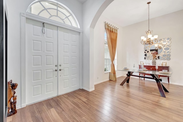 entryway with a chandelier, light wood-type flooring, arched walkways, and baseboards