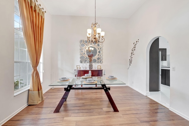 dining area with arched walkways, baseboards, wood finished floors, and a chandelier