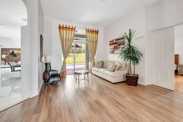 living area featuring arched walkways, baseboards, and light wood finished floors