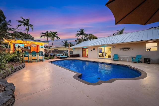 pool at dusk with a patio area, fence, an outdoor pool, and a playground