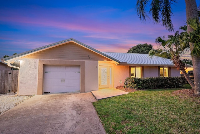 ranch-style home with concrete driveway, metal roof, a lawn, and stucco siding