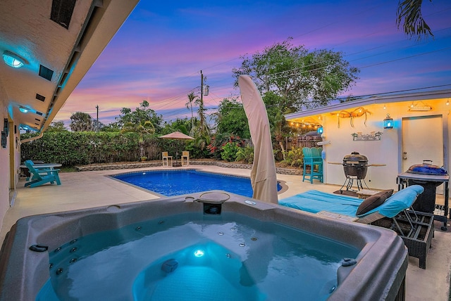 pool at dusk with grilling area, a patio area, fence, and an outdoor hot tub