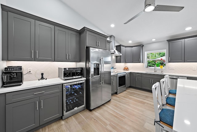 kitchen featuring beverage cooler, a sink, appliances with stainless steel finishes, wall chimney exhaust hood, and light wood finished floors