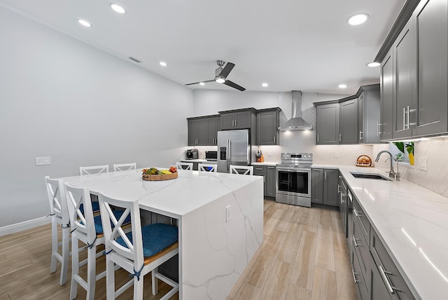 kitchen featuring stainless steel appliances, gray cabinets, decorative backsplash, a sink, and wall chimney range hood