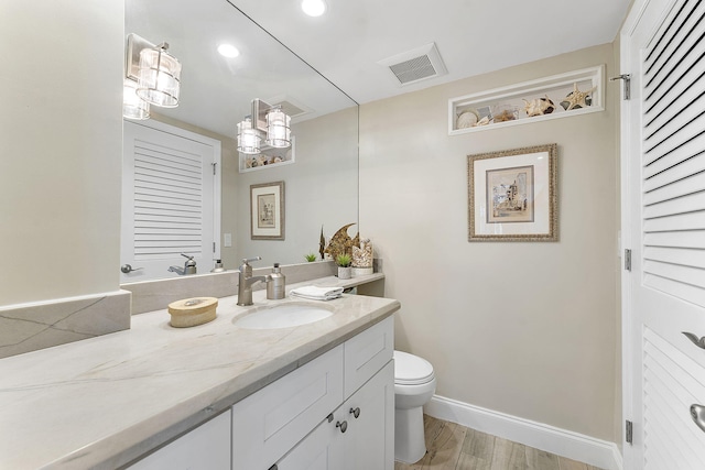 bathroom featuring visible vents, toilet, vanity, wood finished floors, and baseboards