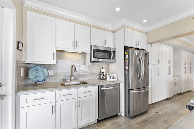 kitchen featuring light wood-style flooring, appliances with stainless steel finishes, ornamental molding, white cabinets, and a sink