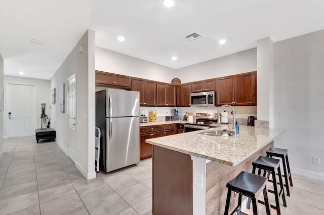 kitchen with visible vents, a breakfast bar, a peninsula, stainless steel appliances, and a sink