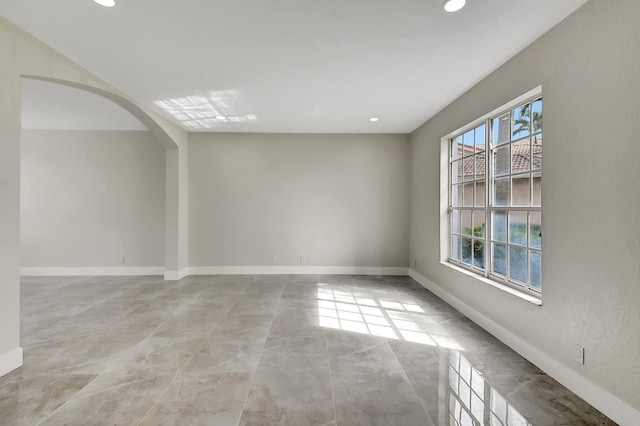 unfurnished room with baseboards, arched walkways, and recessed lighting