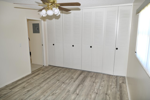 unfurnished bedroom featuring a closet, electric panel, baseboards, and wood finished floors