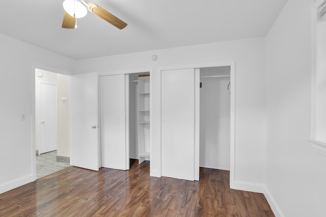 unfurnished bedroom with baseboards, a ceiling fan, multiple closets, and wood finished floors