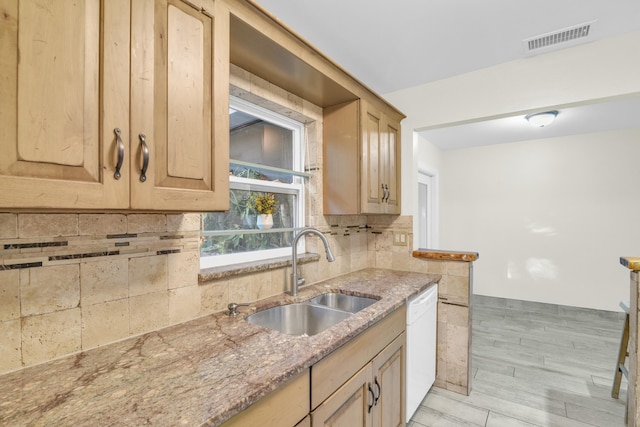 kitchen featuring light stone counters, white dishwasher, light brown cabinets, a sink, and visible vents