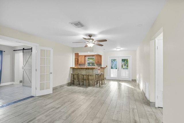 interior space featuring a barn door, visible vents, light wood-style floors, french doors, and a kitchen bar