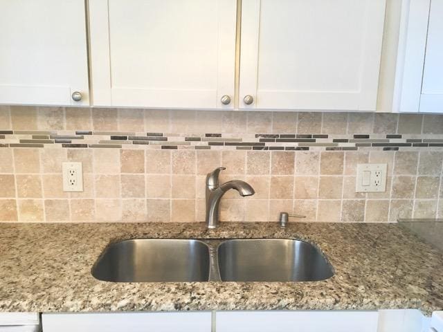 interior details with light stone counters, white cabinets, a sink, and backsplash