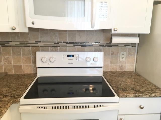 kitchen with white appliances, white cabinetry, backsplash, and dark stone countertops