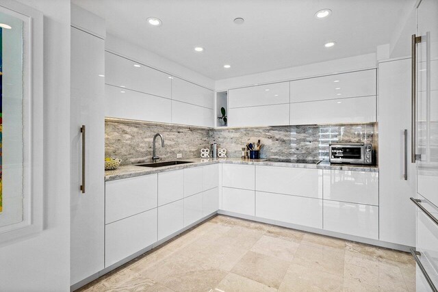 kitchen with modern cabinets, a sink, light stone countertops, and white cabinets