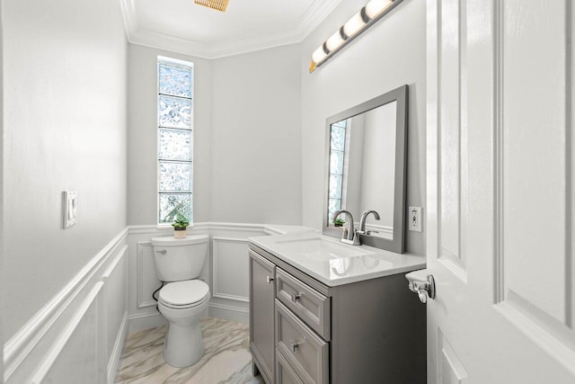 half bathroom with vanity, ornamental molding, wainscoting, a decorative wall, and toilet