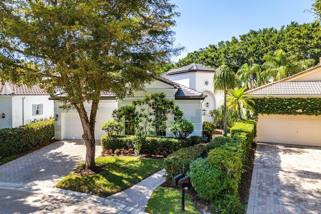 mediterranean / spanish home featuring stucco siding, an attached garage, a tile roof, and decorative driveway