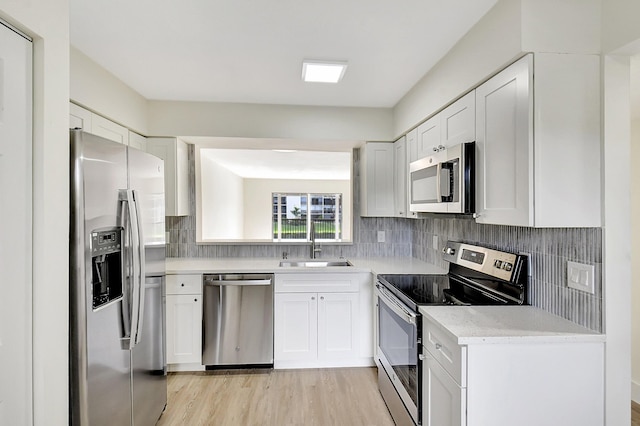 kitchen with backsplash, stainless steel appliances, a sink, and light wood finished floors