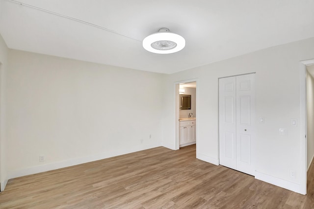 unfurnished bedroom featuring light wood-style floors, ensuite bath, baseboards, and a closet