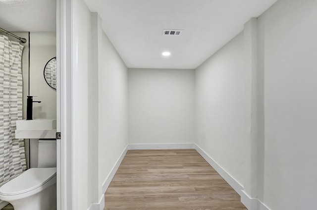 hall featuring a sink, wood finished floors, visible vents, and baseboards