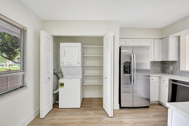 kitchen featuring stainless steel appliances, light countertops, stacked washer and clothes dryer, and white cabinetry