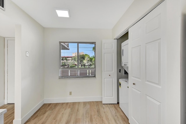 laundry room featuring laundry area, baseboards, light wood-style floors, and stacked washer and clothes dryer