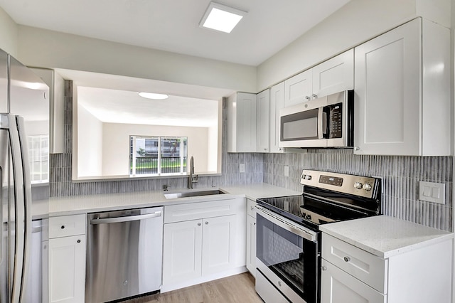 kitchen with appliances with stainless steel finishes, a sink, white cabinetry, and tasteful backsplash