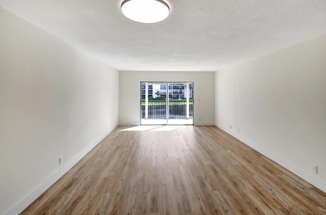 empty room with a textured ceiling, baseboards, and wood finished floors