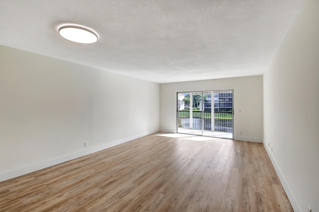 empty room featuring light wood-style floors, a textured ceiling, and baseboards