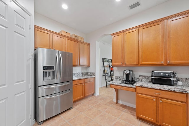 kitchen featuring arched walkways, light tile patterned floors, light stone counters, visible vents, and stainless steel fridge with ice dispenser