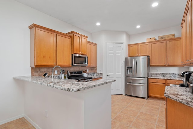 kitchen with light stone counters, backsplash, appliances with stainless steel finishes, a sink, and a peninsula