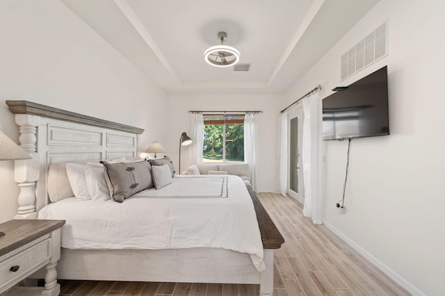 bedroom featuring visible vents, a tray ceiling, and wood finished floors