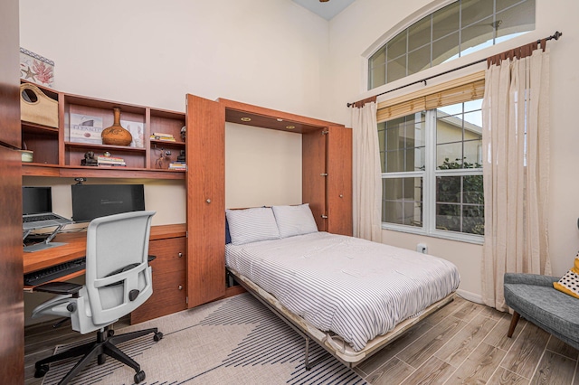 bedroom featuring a towering ceiling, baseboards, and wood finished floors