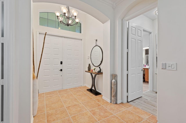 entrance foyer featuring light tile patterned floors, baseboards, arched walkways, crown molding, and a notable chandelier