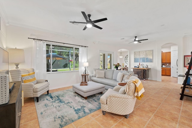 living area with ornamental molding, arched walkways, light tile patterned flooring, and ceiling fan