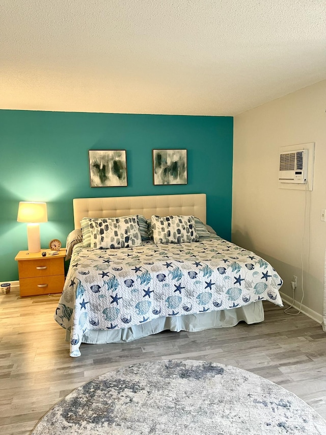 bedroom with a wall mounted air conditioner, a textured ceiling, baseboards, and wood finished floors