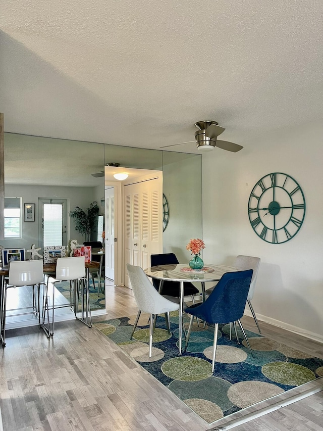 dining area featuring a ceiling fan, a textured ceiling, baseboards, and wood finished floors