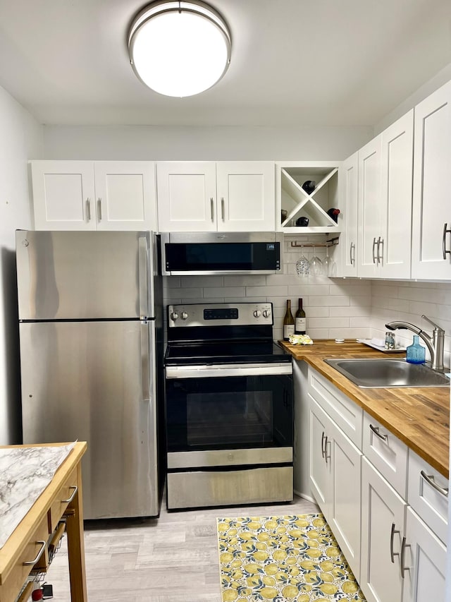 kitchen with stainless steel appliances, tasteful backsplash, butcher block counters, white cabinets, and a sink