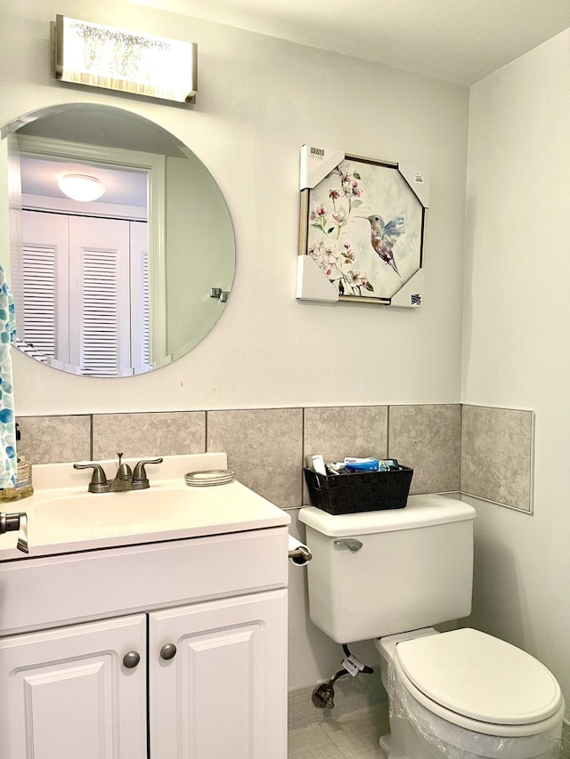 bathroom featuring a wainscoted wall, tile walls, toilet, vanity, and tile patterned flooring