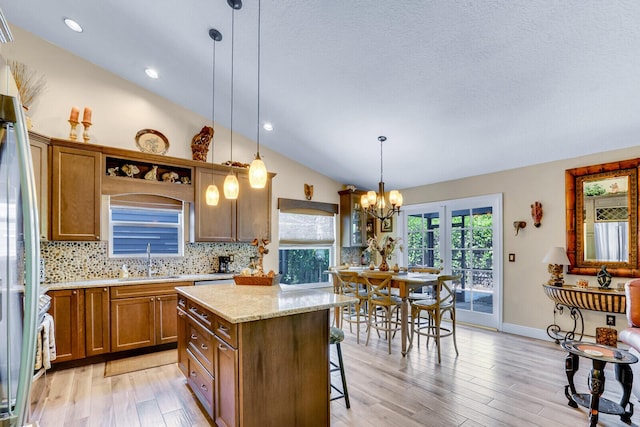 kitchen featuring lofted ceiling, a sink, light wood-style floors, decorative backsplash, and brown cabinetry