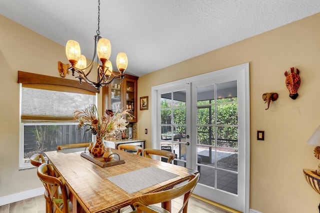 dining area with a textured ceiling, a notable chandelier, baseboards, light wood-style floors, and french doors