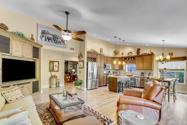 living area with a textured ceiling, high vaulted ceiling, ceiling fan with notable chandelier, visible vents, and light wood-style floors